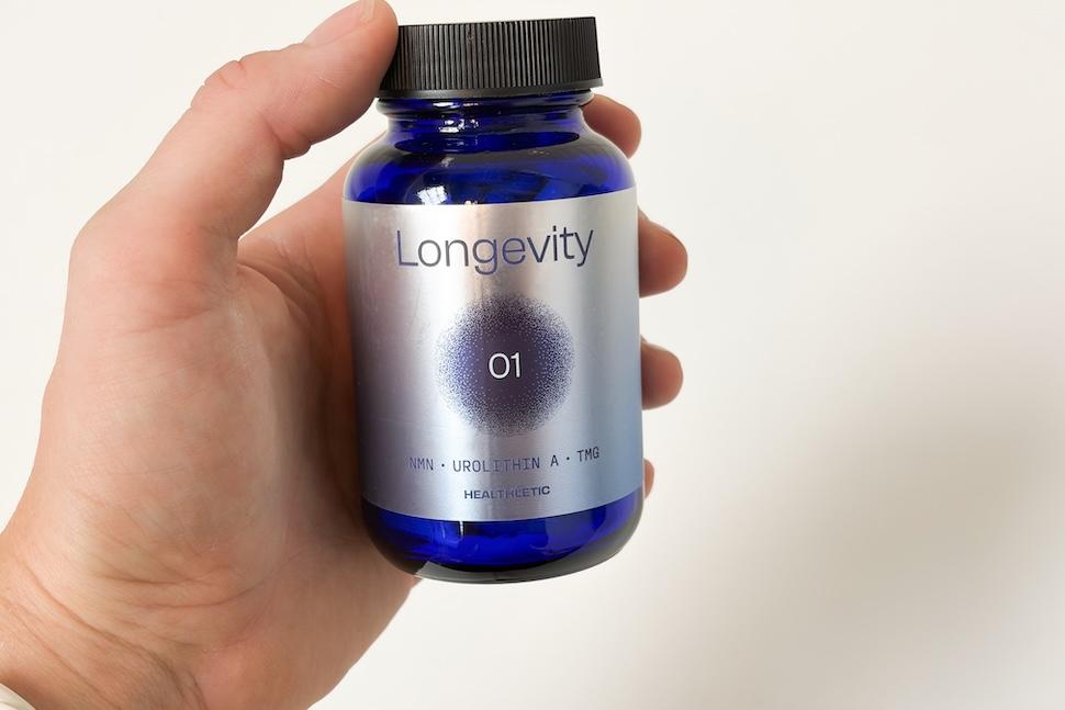 Closeup of a hand holding a bottle of Healthletic Tri-Active Cellular Longevity Complex