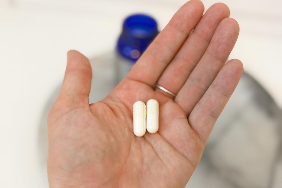 Closeup of a hand holding two off-white capsules of Tru Niagen 1,000