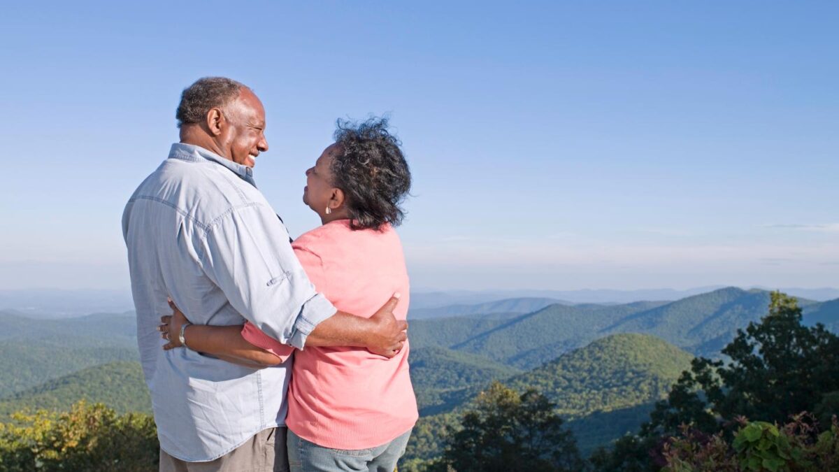 Senior couple embracing on hill, smiling at each other